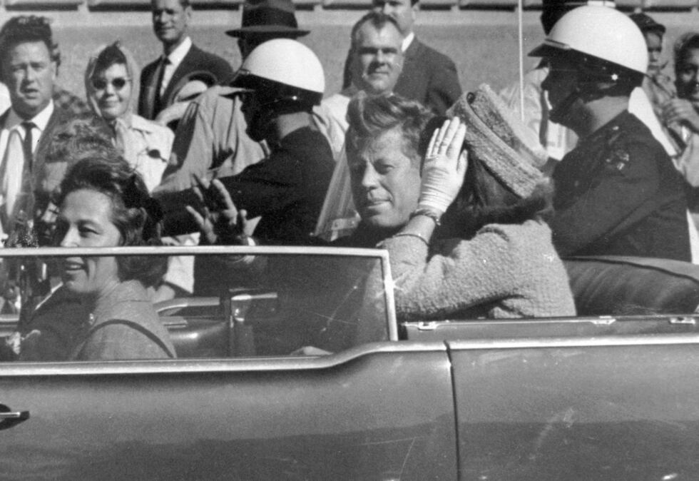 FILE - President John F. Kennedy waves from his car in a motorcade approximately one minute...